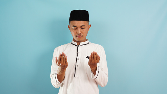 Asian muslim man praying gesture on light blue background