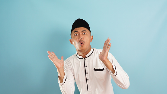 shocked, startled, surprised expression a muslim man caused good news on blue light background