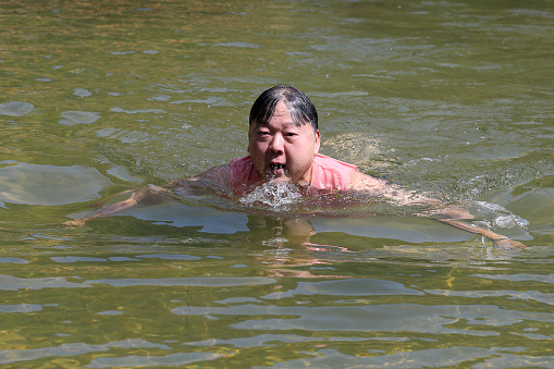 An Asian senior man is spending time swimming at public pool in nature reserve