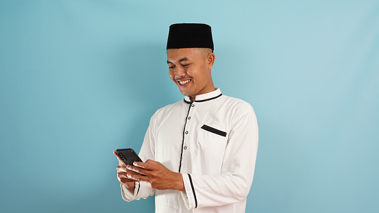 A muslim man excited get good news from phone, celebrating success on blue background