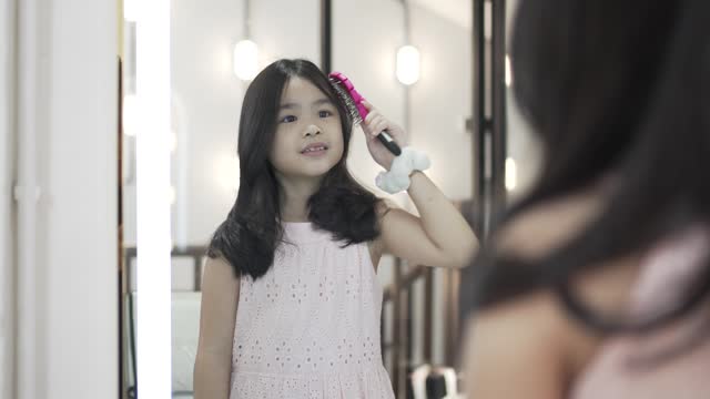 Kid combing her hair in front of mirror in salon