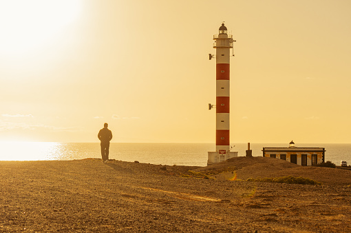 A picture of a man's silhouette while walking near the Lighthouse at the Poris in Tenerife. The hard warm light from the sunrise hitting the sea.
