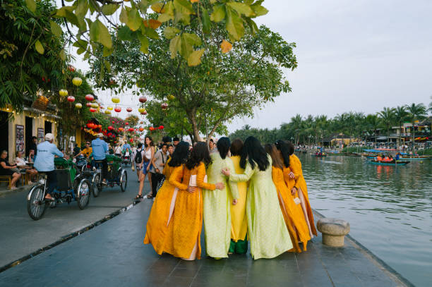 Hoi An, Vietnam - 20 February 2024: A group of Vietnamese women are dressed in traditional clothing, the Ao Dai. They pose for a group photo in front of the backdrop of the historic old town adorned with lanterns.