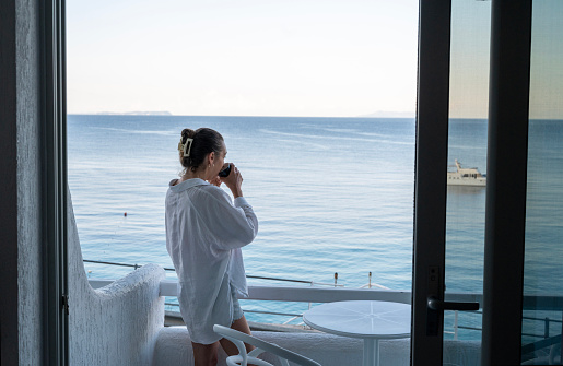 Woman enjoys morning coffee on balcony over sea