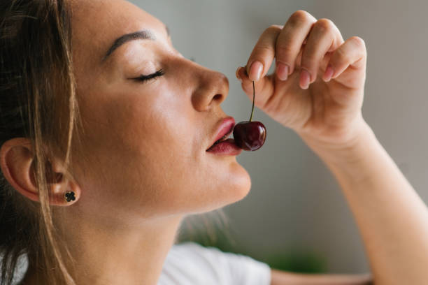 Attractive young woman eats fresh cherry, healthy berry close-up