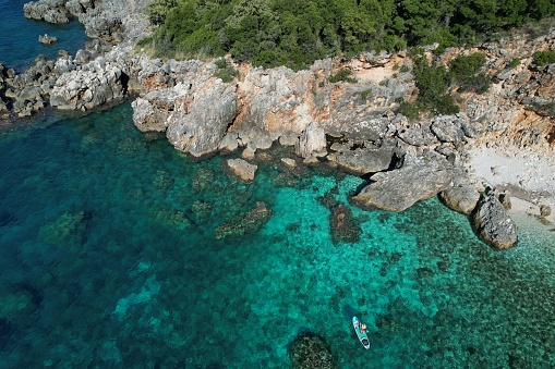 Aerial view of woman paddle boarding on turquoise coloured sea and rugged coastline
