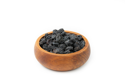Black Raisins in wooden bowl isolated on white. Dried fruits.