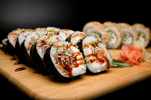 picturesque scene unfolds, featuring rolls with tuna, salmon, cucumber, and tobiko caviar. In the background, a set with classic additions of ginger and wasabi, sprinkled with sesame seeds, and drizzled with sweet and sour sauce.