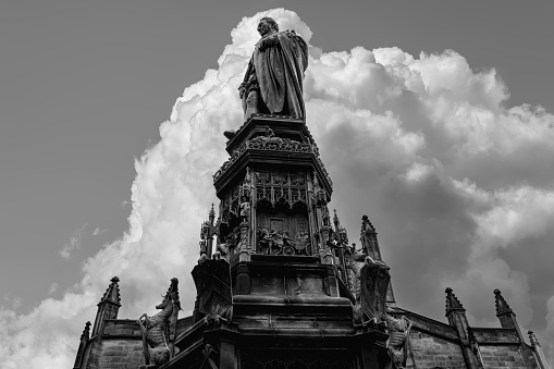 A black and white image showcases the statue of Walter Francis Montagu Douglas Scott, Duke of Buccleuch, against an imposing backdrop of cumulus clouds