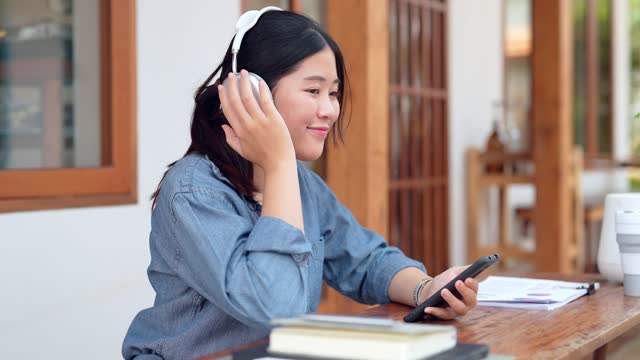 An Asian female entrepreneur is unwinding at a nearby cafÃ©, selecting songs on her smartphone, and listening to music through her headphones, enjoying a relaxing break from work
