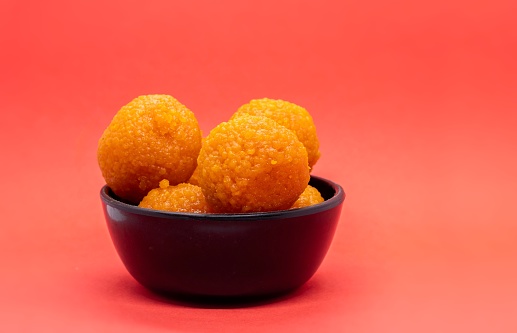 Indian Sweet Motichoor Laddu or Motichur Ladoo in a Black Bowl Isolated on Red Background with Copy Space, Also Known as Bundi Ladoo.