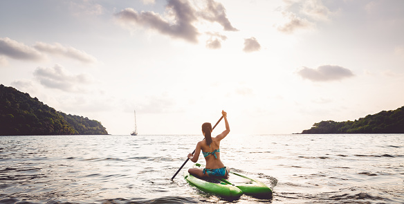 Travel asian woman with bikini relax and playing on paddle board in sea at Koh Kood, Thailand, evening time, summer vacation concept