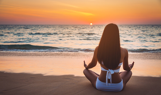 Summer woman vacation concept, Travel asian woman with white bikini practicing yoga meditation on sea beach in Phuket, Thailand