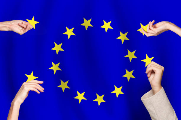 Hands place yellow stars in a circle on a blue background resembling the European Union flag.