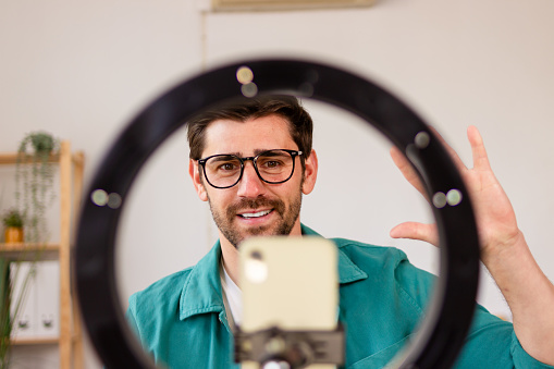 Smiling man recording a video with a smartphone mounted inside a ring light