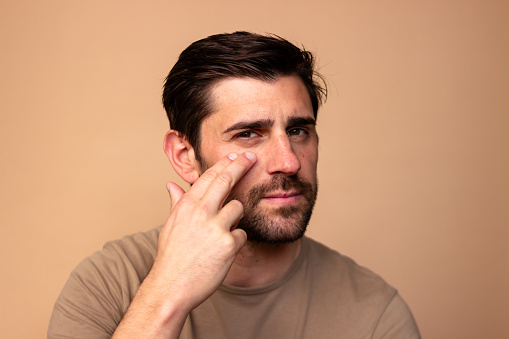 Young adult male examining facial skin in close-up mirror inspection for skincare routine and personal grooming. Checking for blemishes. Signs of aging. And overall skin health and wellness