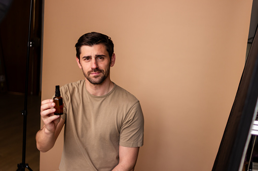 Young man holding a bottle of serum, showcasing beauty product against a plain background