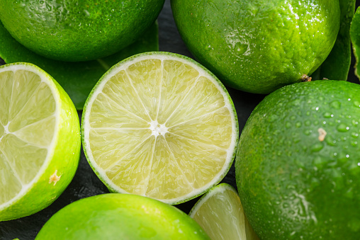 Ripe lime fruits with slices and lime leaves on a gray stone table. Nice fruit citrus background for your projects.