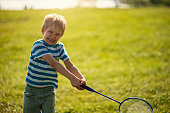 Funny and cute little boy playing badminton on a beautiful grass field on sunset.