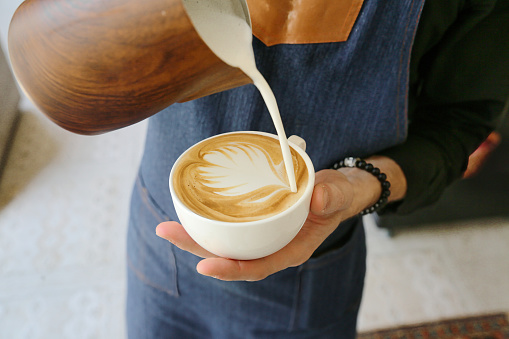 A person pours milk into a cup of coffee, creating a creamy blend of flavors.