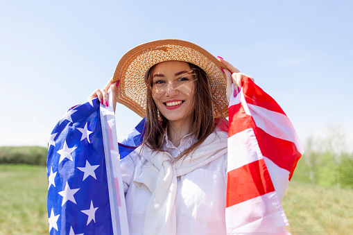 cute girl standing on the grass and holding american flag in field on the lawn and looks into the distance, fourth of july concept