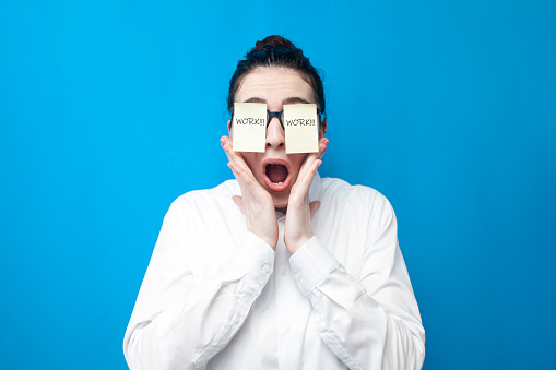 shocked woman manager screaming in stress on blue background, girl office worker with papers in front of her eyes surprised, the concept of deadlines