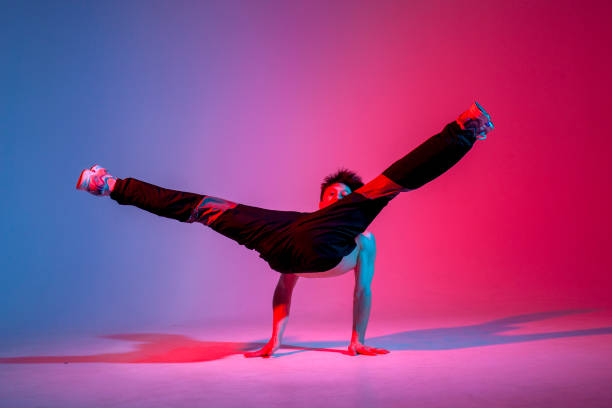 istock young guy dancer in black clothes break dancing in neon lighting, man performs hip hop movement in red blue club 2106349257