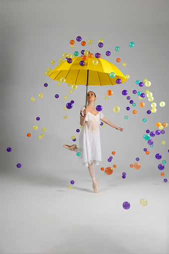 Colorful balls are raining from the sky. Beautiful ballerina is protected from colorful balls with her Japanese umbrella.