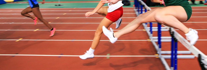 Girls running over hurdles indoors