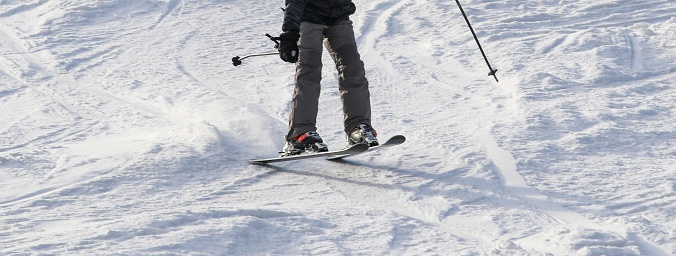 An individual skier is captured in mid-glide as they navigate a gentle descent on a well-trodden snowy ski slope