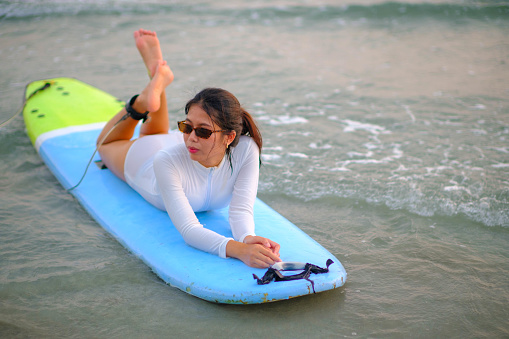 Young Asian woman lying on a surfboard at the sea in the evening