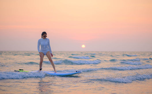 Young Asian woman stands surfing by the sea in the evening when the sun sets.