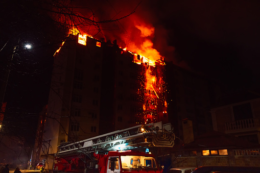Fire truck and burning house is engulfed in flames at night. Fire blazing in apartment building.