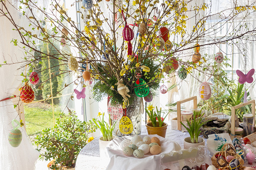 Easter eggs decorations, feathers and pussy willow twigs with catkins in a vase. Beautiful defocused lights bokeh. Space for copy.