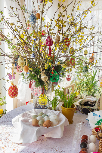 Tree branches decorated with Easter eggs in a vase on the dining table in a bright room