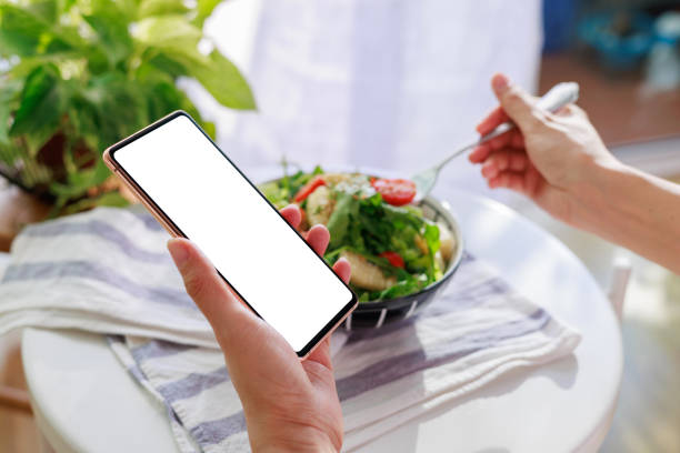 istock A woman's hand holding a smartphone while enjoying salad at home, with the smartphone displaying a blank screen for design mockup. 2106533103