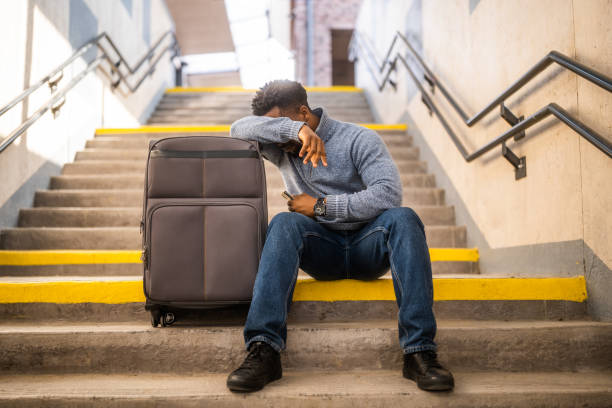 Worried man with a phone and suitcase sitting on a stairs at the railway station.