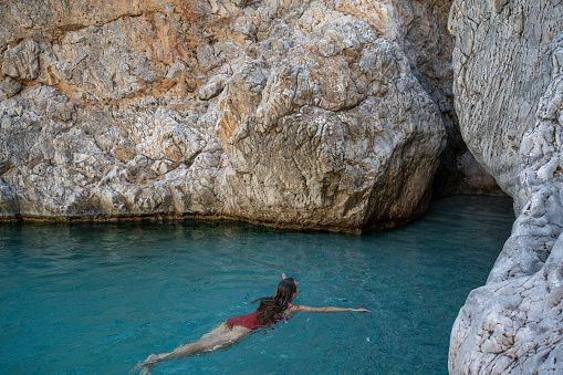 Woman swims between cliffs in turquoise sea