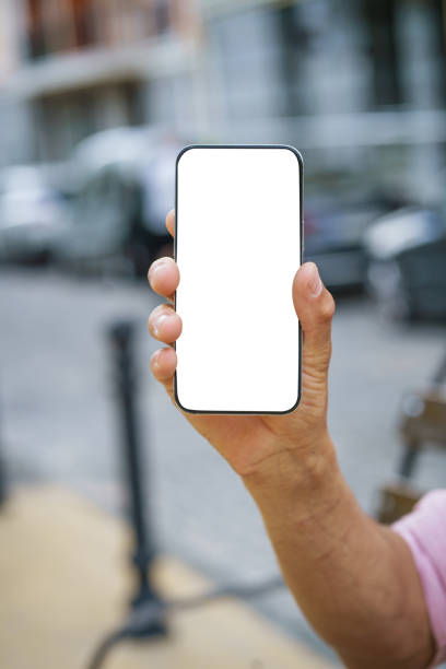 istock Close-up of man's hand holding mobile phone with white screen display, offering ample copy space. Background features urban cityscape, providing modern and vibrant backdrop. 2106613198