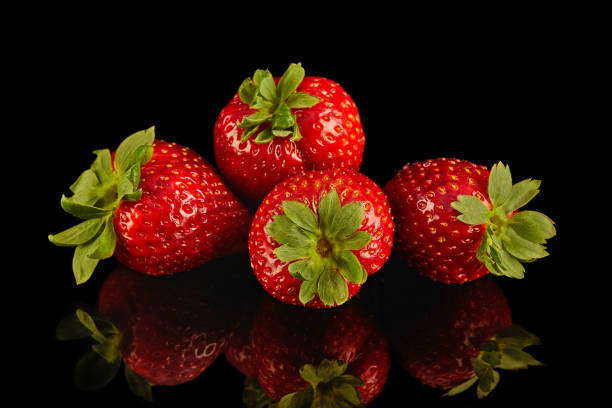 Four strawberries rest on black surface, vibrant produce from natures bounty