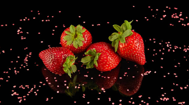 Four strawberries rest on black surface, vibrant produce from natures bounty