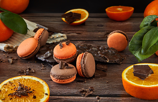 Delicious chocolate-flavored macaroons with orange on a dark wooden background and green leaves. Ideal image for pastries, desserts or food blog content.