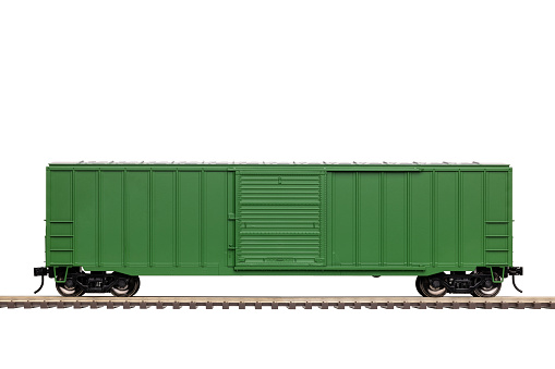 A green railroad box car with closed door on railroad track.