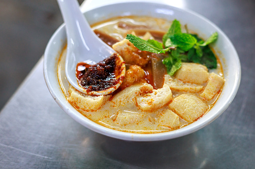 Penang's famous Curry Mee is a flavorful dish served with coagulated pig's blood, prawn, cuttlefish, cockles and topped with spicy chili paste