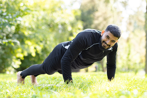 Active man in sportswear engaged in push-ups, showing strength and fitness at a sunny, green park.