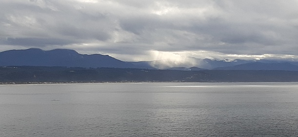 Minimalistic, almost monochromatic photos reflecting silver sunlight on the tranquil Indian Ocean off the coast of Plettenberg Bay. Sunbeams steam down on the distant mountains that are cloaked in cloud. The heavy clouds are indicative of the inevitable rainfall.