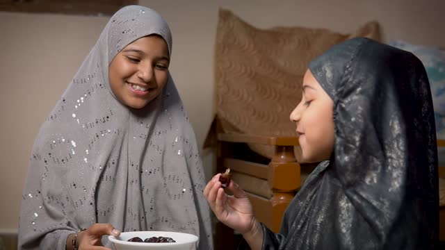 Two happy Islamic girls in hijab eating dates fruits during Ramadan.