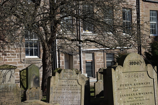 Old gravestones in the Howff cemetery in Dundee, Scotland, with an old tenement building in the background