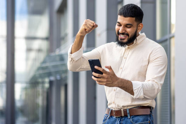 istock Joyful man celebrating success with smartphone in urban setting 2106711267
