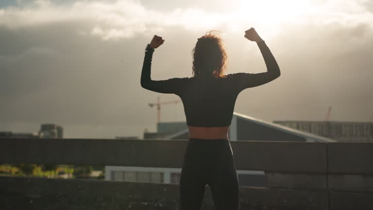 Fitness, city and back of woman celebration for cardio time, running success or workout goals, fist or achievement. Morning wellness, watch check and excited runner, athlete and celebrate on bridge